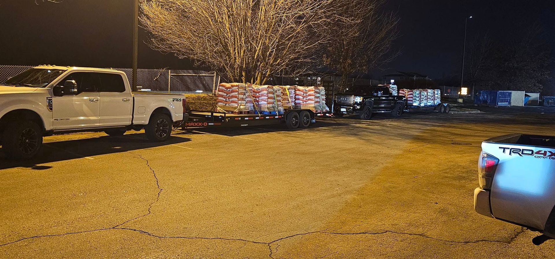 White truck towing a trailer with stacked materials parked at night near a dark building.