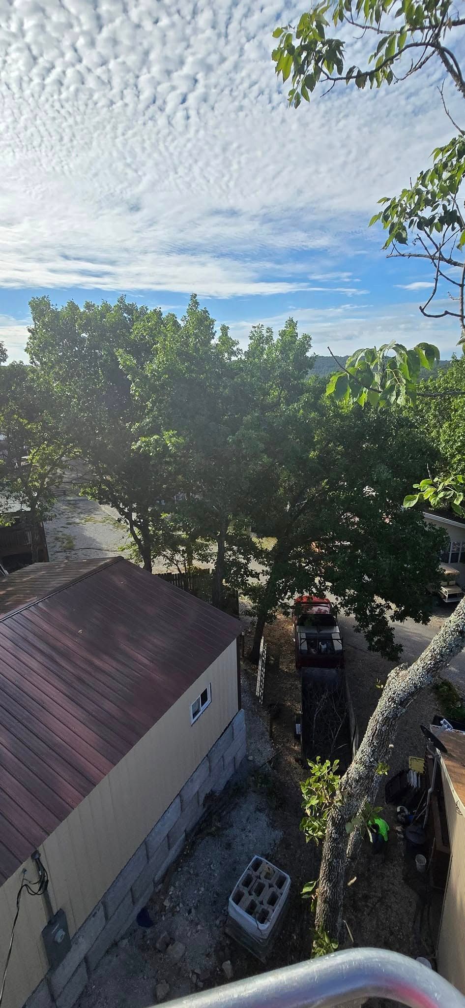View from above, a building with a red roof, green trees, and a cloudy blue sky.