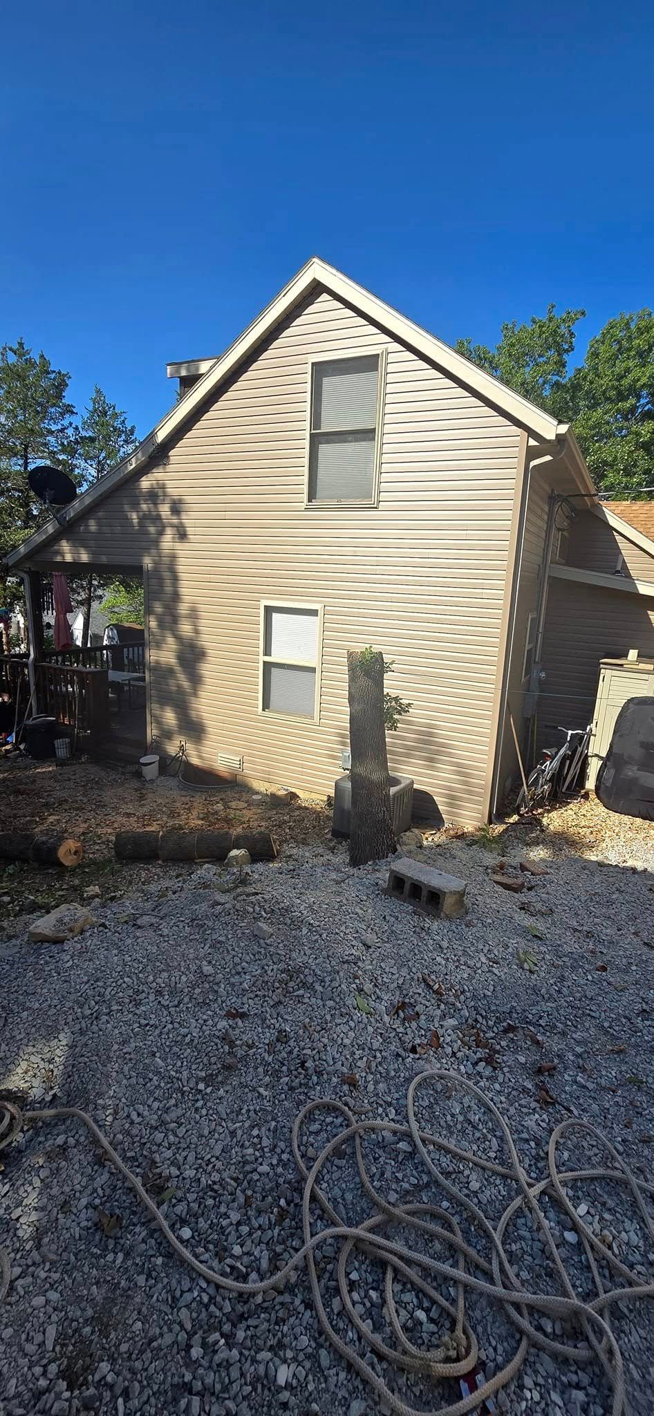 Side view of a weathered house with a gravel yard under a bright blue sky.