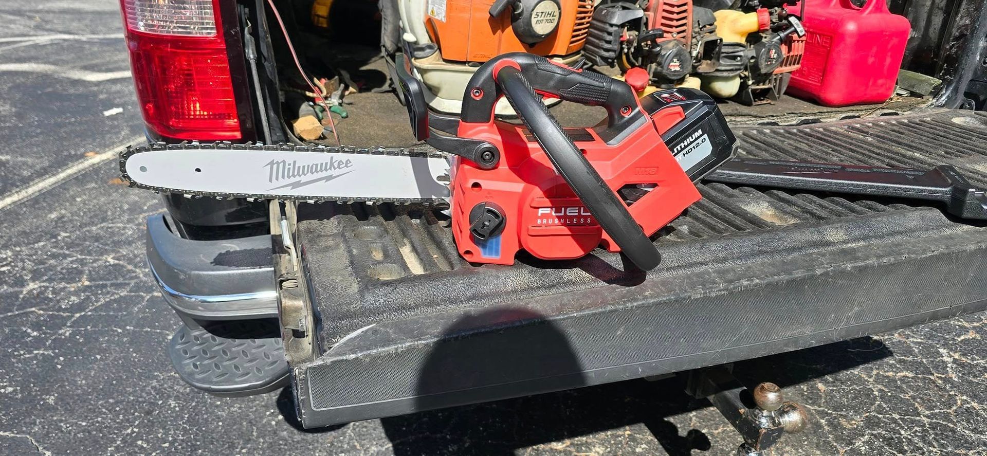 Red chainsaw on the tailgate of a truck. Other tools and equipment are in the truck bed.