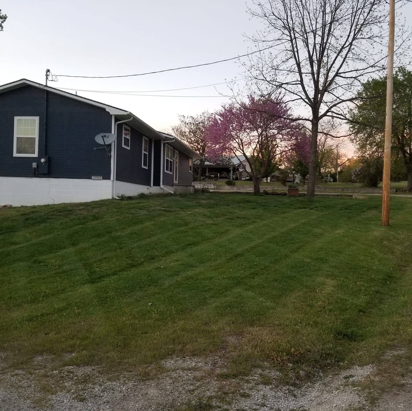 A dark blue house with a well-manicured lawn and a blooming pink tree.