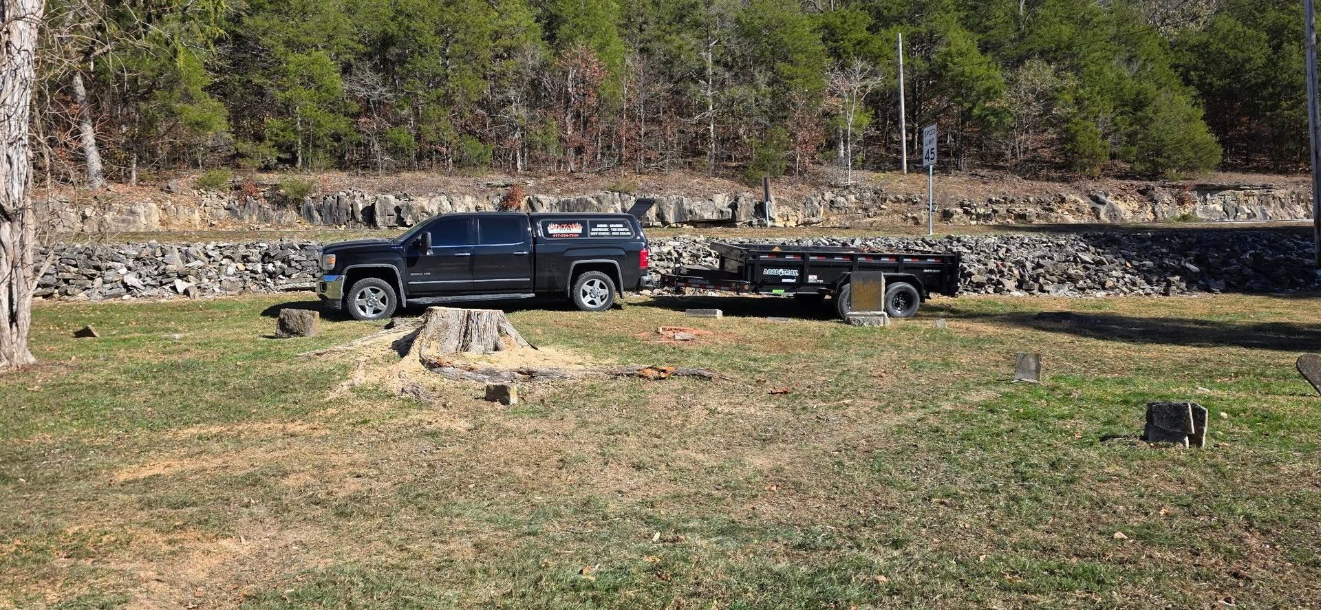 Black truck towing a trailer on a grassy area, trees in the background.