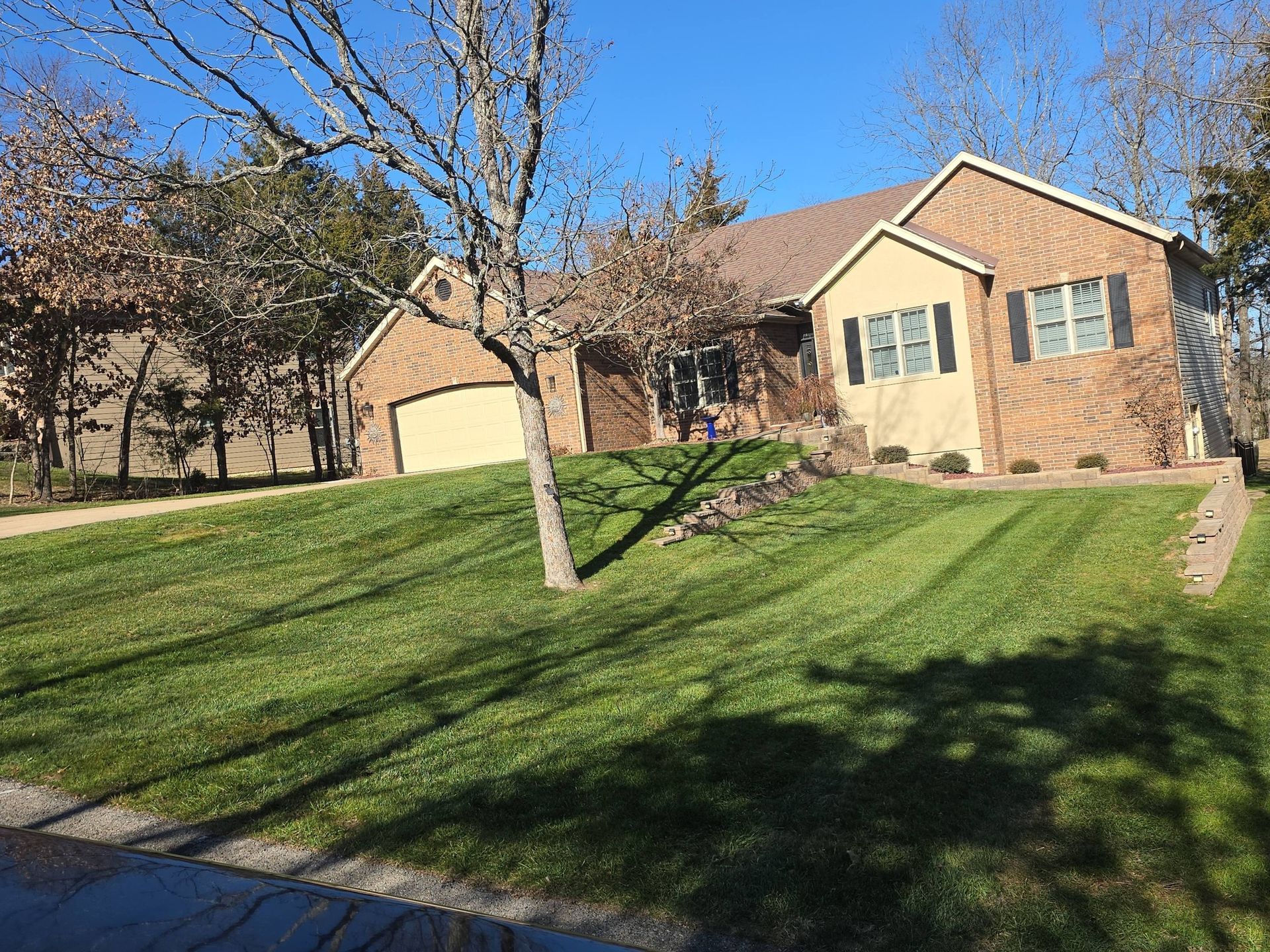 House with a lawn, driveway, and tree in front on a sunny day.