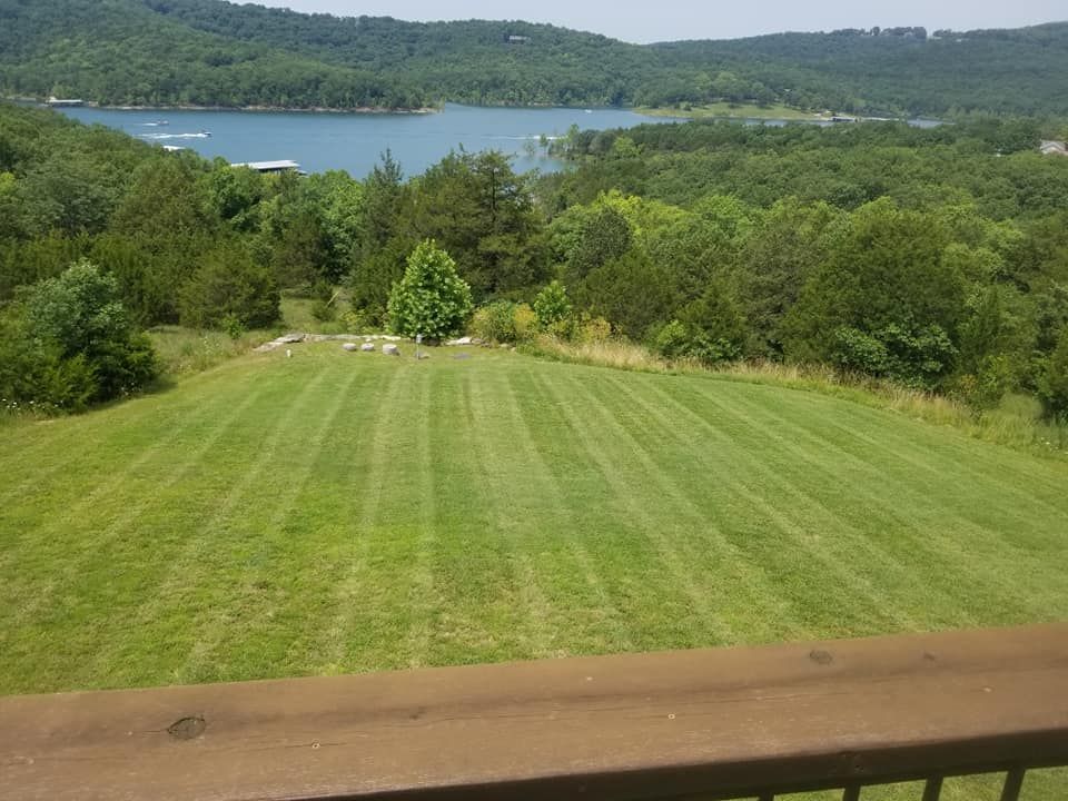 Lush green lawn with freshly cut stripes overlooks a lake surrounded by trees and mountains.