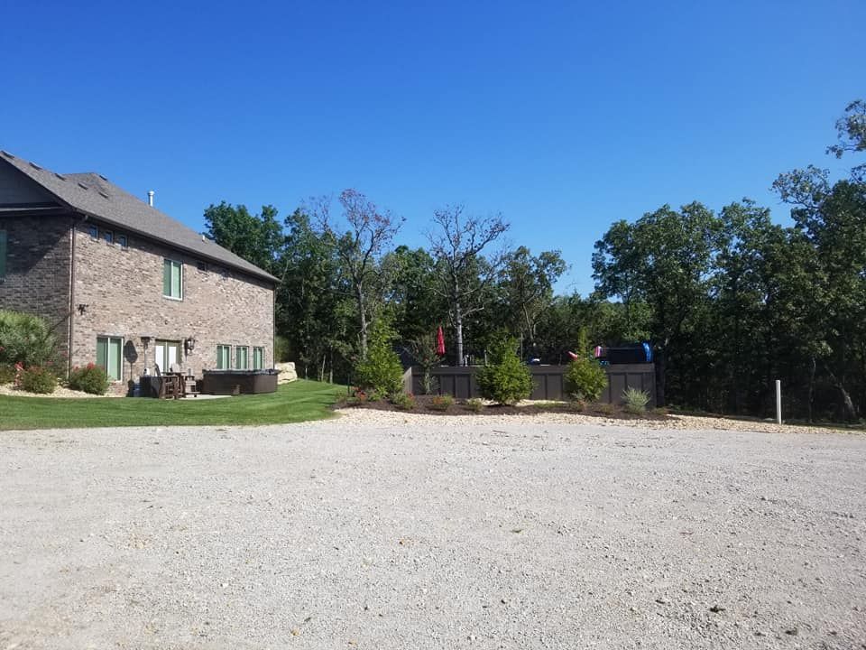 A gravel parking area next to a two-story brick building, with trees in the background under a blue sky.