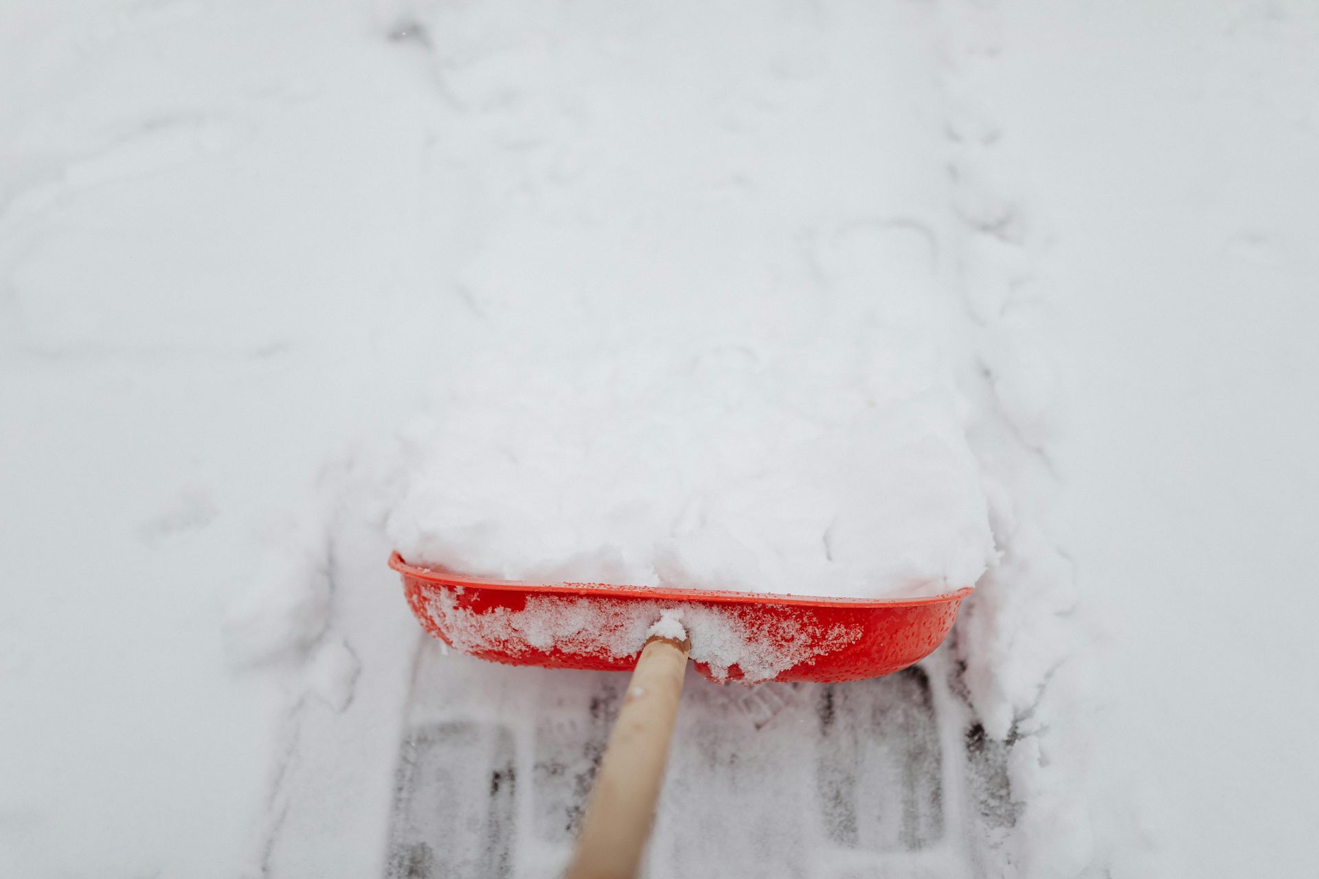 Red snow shovel clearing snow from a brick surface.