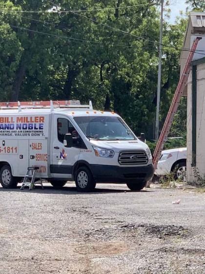 White service van parked on a gravel lot beside a building, with trees in the background.