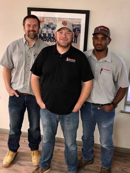 Three people standing indoors in front of a framed picture, wearing company shirts and jeans.