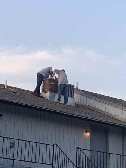 Two workers on a rooftop installing or repairing a vent pipe.