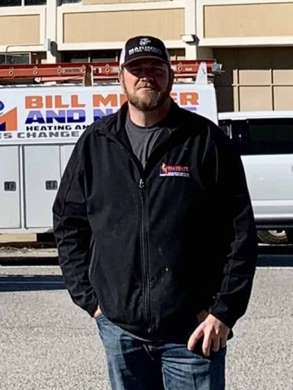Man in black jacket and cap standing in front of a Bill Miller Heating & Cooling truck