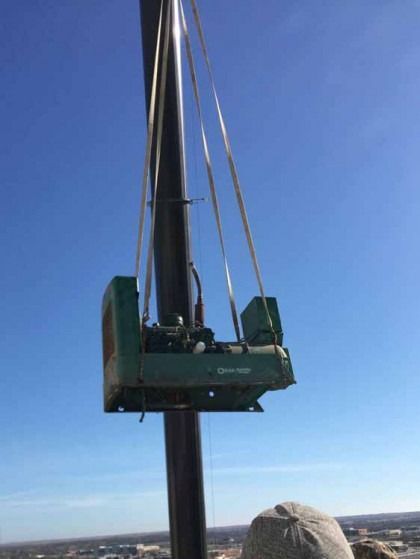 Green industrial platform on a tall black tower against a blue sky, with a person in a hard hat at the base