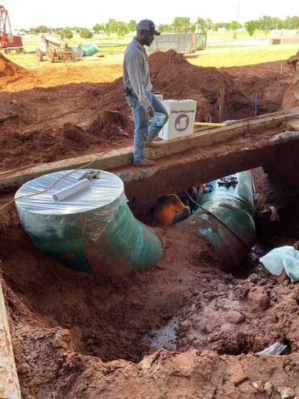 Worker standing in a muddy trench beside large green pipes under construction