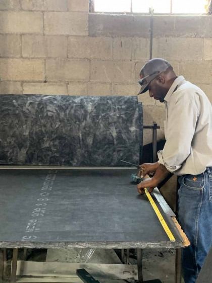Person measuring a large black sheet on a worktable in a workshop.