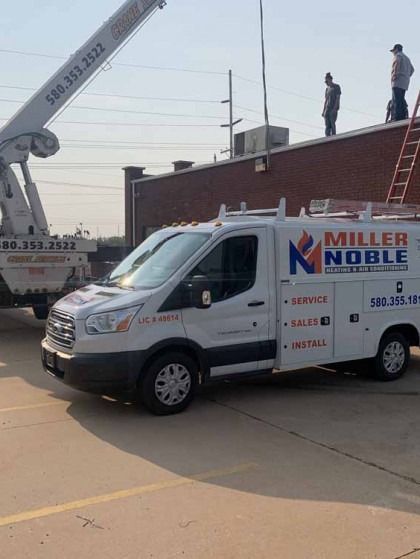 White Miller Noble service van parked by a brick building with a crane and workers on the roof