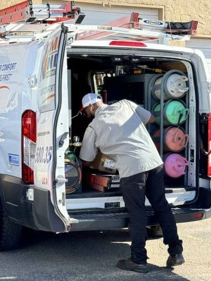 Worker loading equipment into a white utility van with open rear doors and colorful cylinders inside