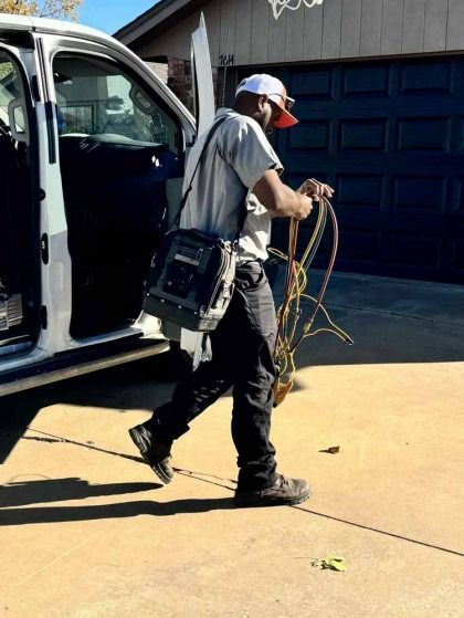 Worker carrying cables beside a white van on a sunny driveway