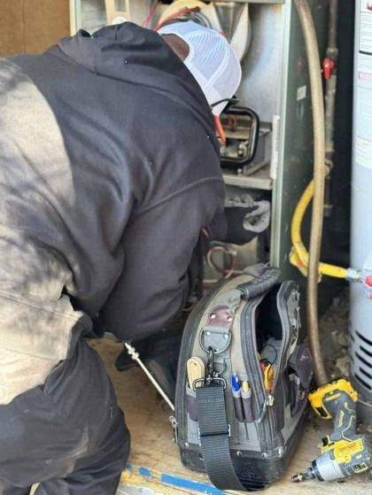 Technician working inside an HVAC unit beside tools and a yellow drill in a utility area