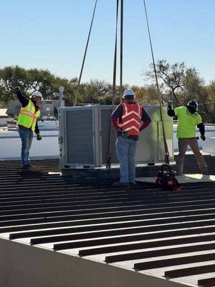 Workers guiding a large rooftop unit being lifted by crane onto a building roof