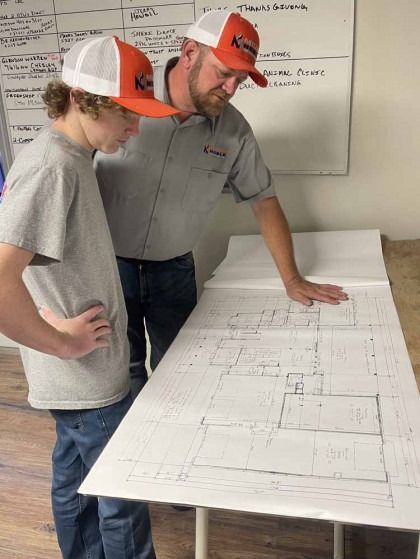 Worker and child reviewing blueprints on a table in a construction office