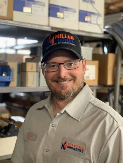 Smiling man in glasses and cap standing in a workshop with shelves and tools behind him