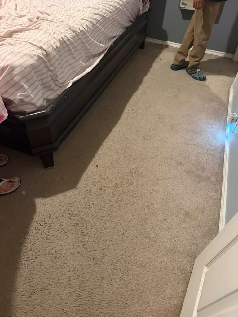 Carpeted bedroom with a bed on the left and a person’s legs standing near the wall.