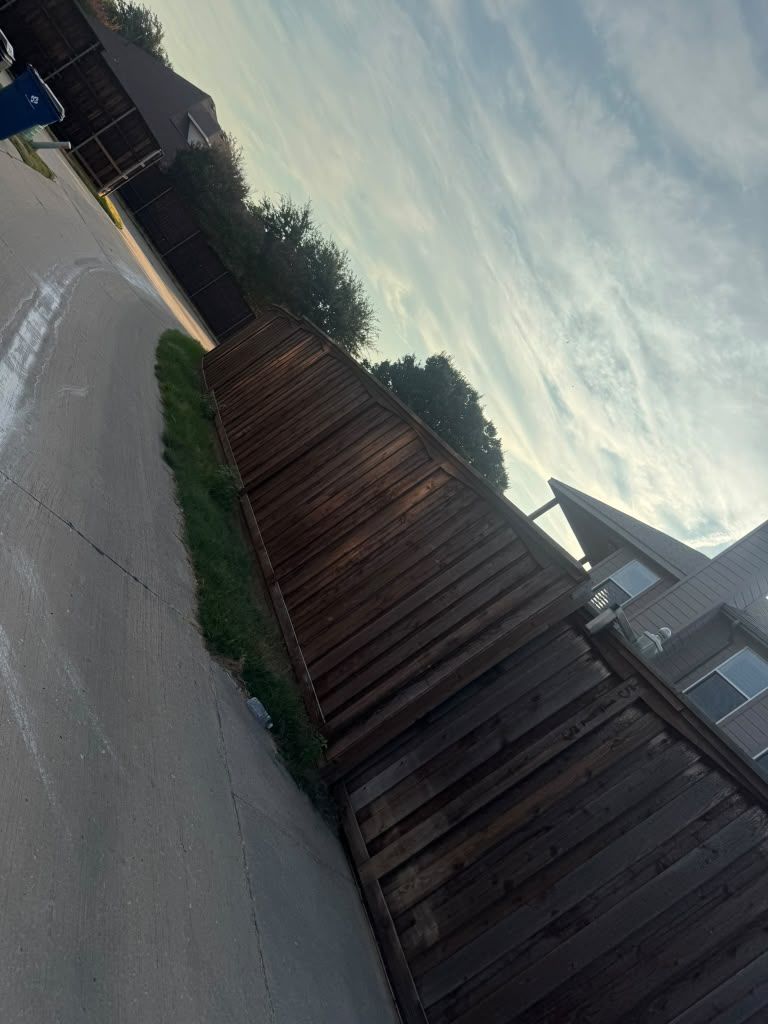 Tilted view of a quiet residential street with a wooden fence, driveway, and cloudy sky at dusk