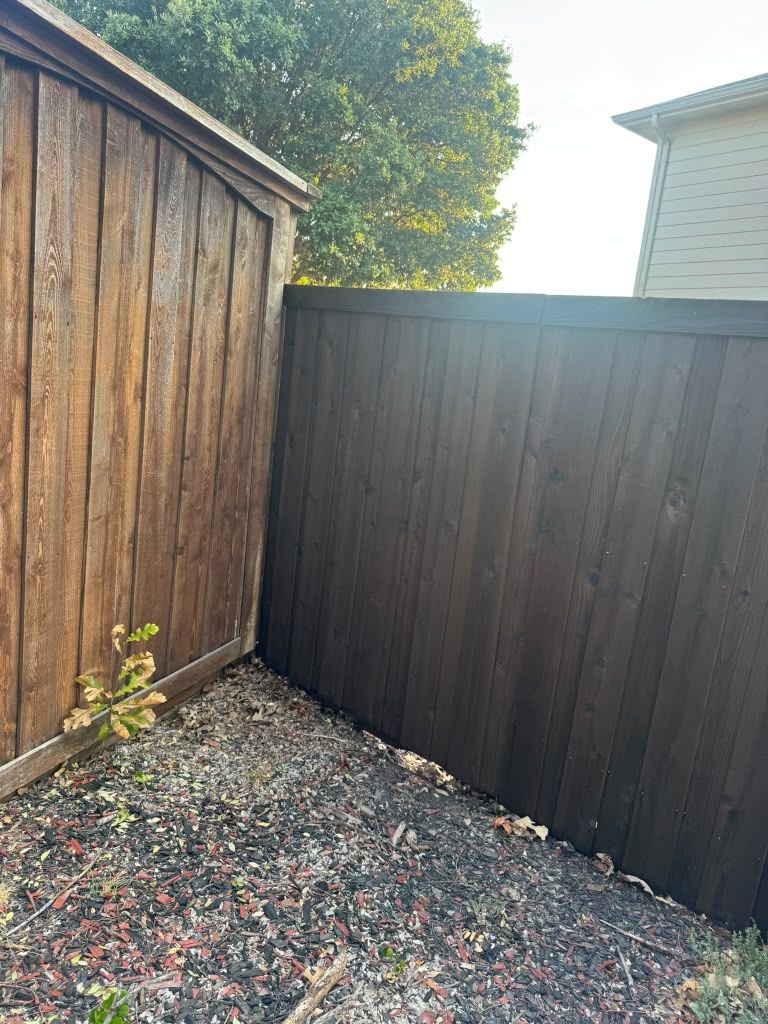 Corner of a fenced gravel yard with wooden sheds and a small plant by the left fence