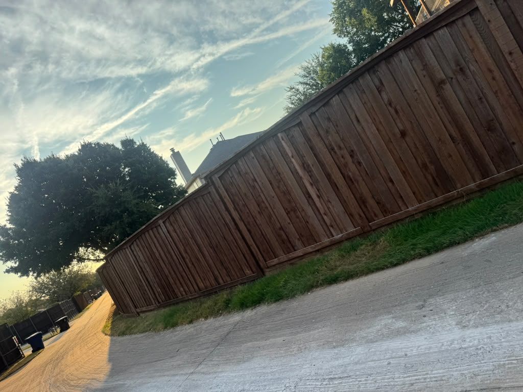Tilted view of a wooden fence beside a gravel road at sunset, with trees and a partly cloudy sky.