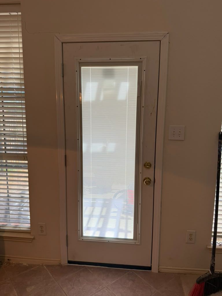 White front door with glass panel beside window blinds in a beige room