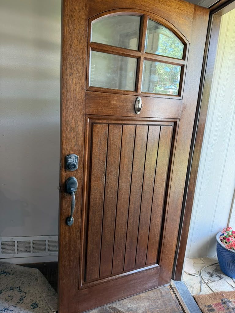 Wooden front door with glass panes and dark hardware, viewed from inside a home