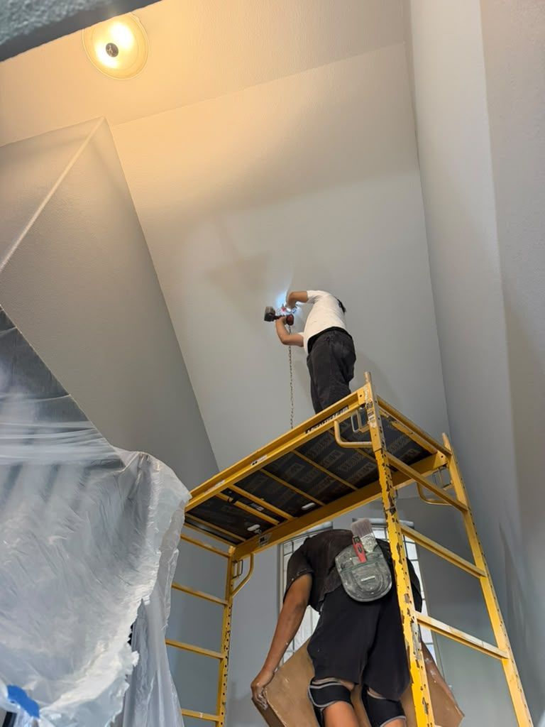 Two workers on a yellow scaffold installing or repairing a white ceiling indoors