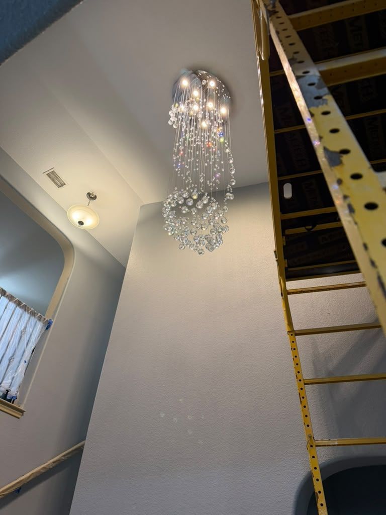 Tall interior stairwell with chandelier on a high ceiling and a yellow ladder leaning on the right wall.