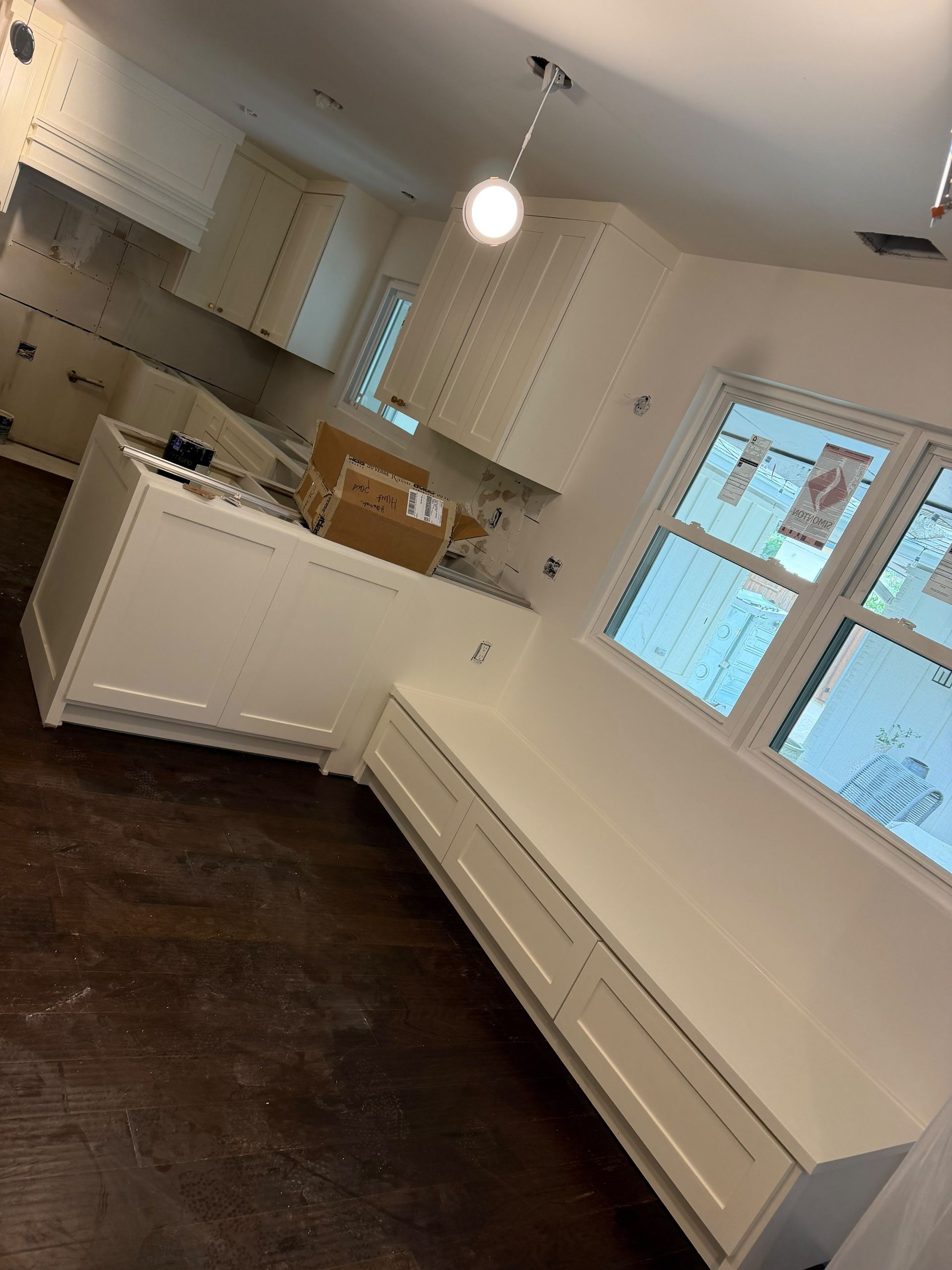 Bright modern kitchen with white cabinets, dark wood floor, and windows letting in daylight.