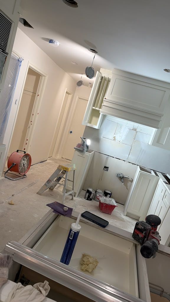 Tilted view of a bright kitchen with white cabinets, a sink, countertop items, and cleaning tools.