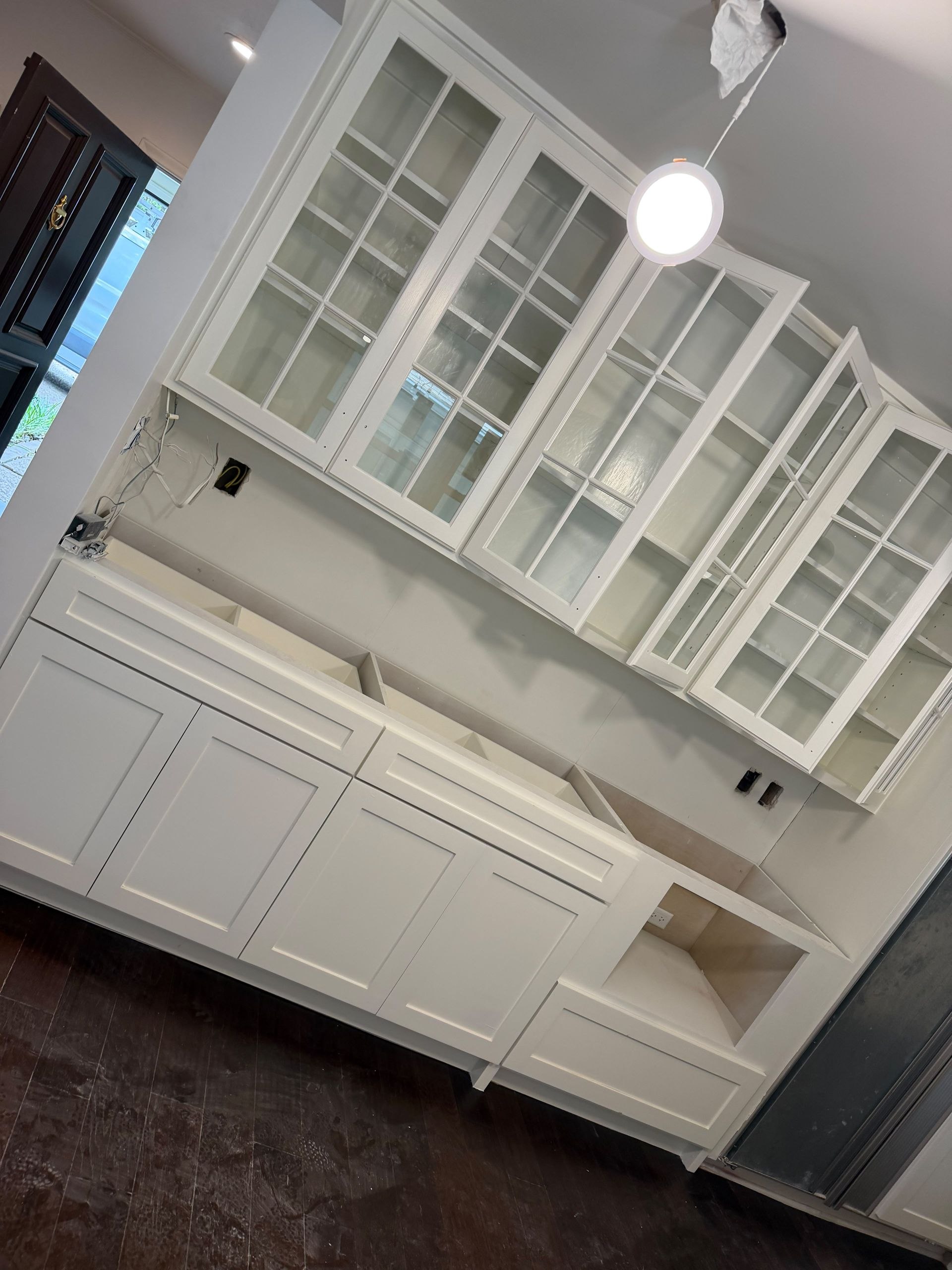 White built-in kitchen cabinets with glass-front uppers and dark flooring, slightly tilted view
