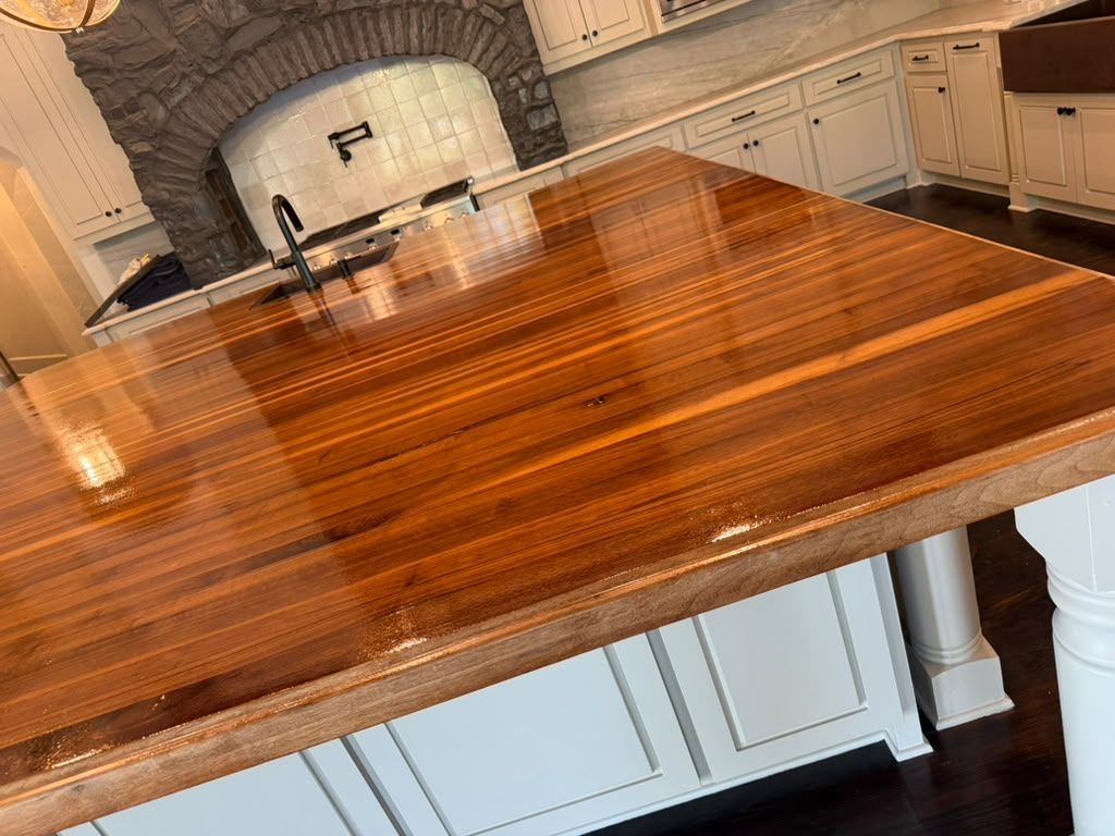 Glossy wooden kitchen island countertop in front of a white built-in oven and cabinets