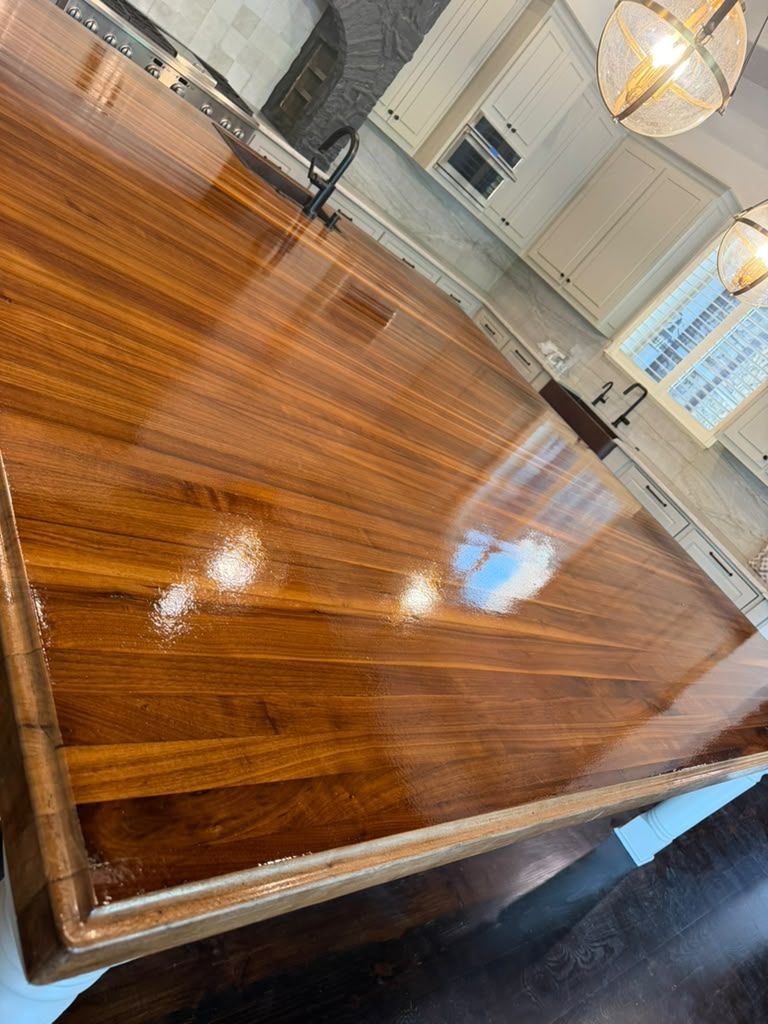 Glossy wooden table in a bright room with white cabinets and hanging lights reflected on the surface