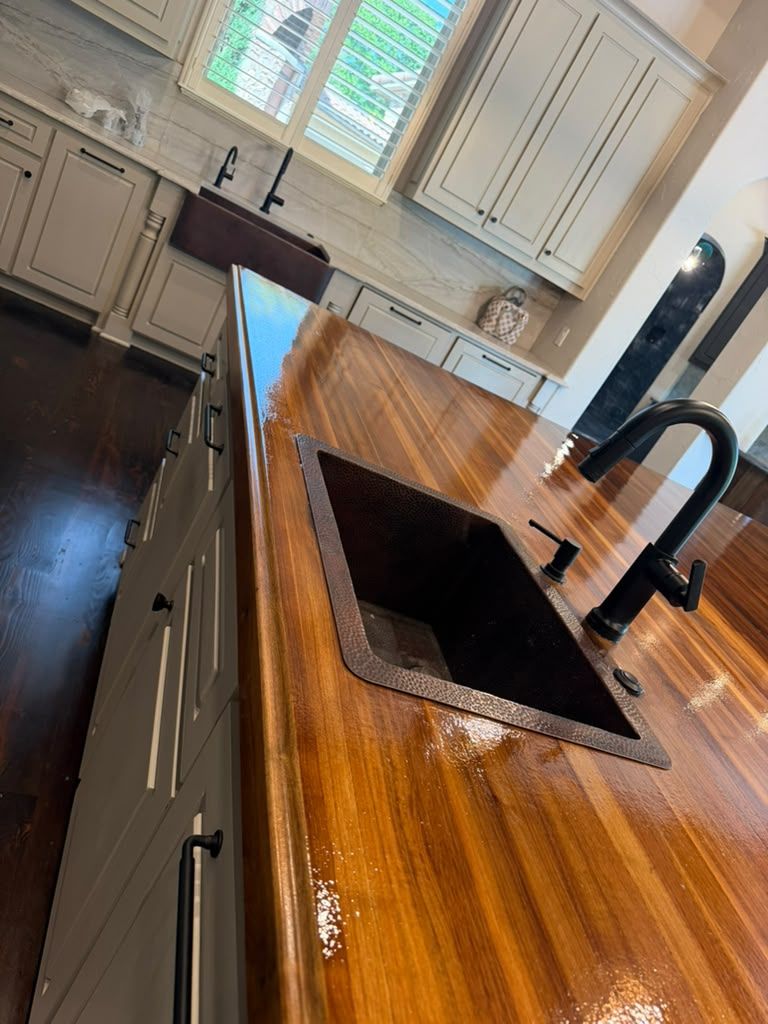 Bright kitchen with a wooden island, black sink and faucet, white cabinets, and windowed walls.
