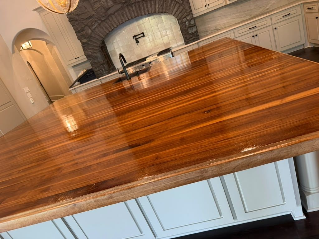 Polished wooden kitchen island with white cabinetry and a stone arch fireplace in the background
