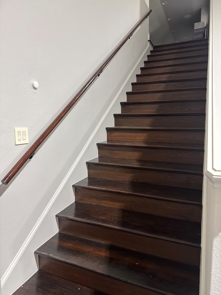 Dark wooden staircase with a metal handrail in a plain indoor hallway