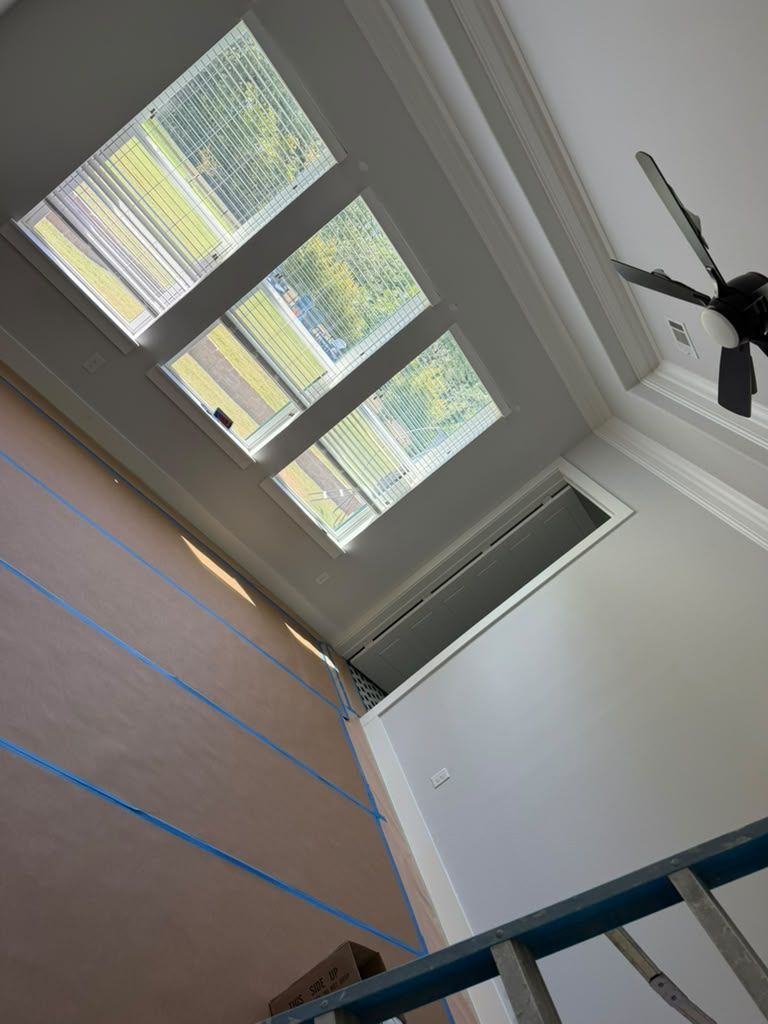 Tilted view of a room with large windows, white walls, and a ceiling fan overhead