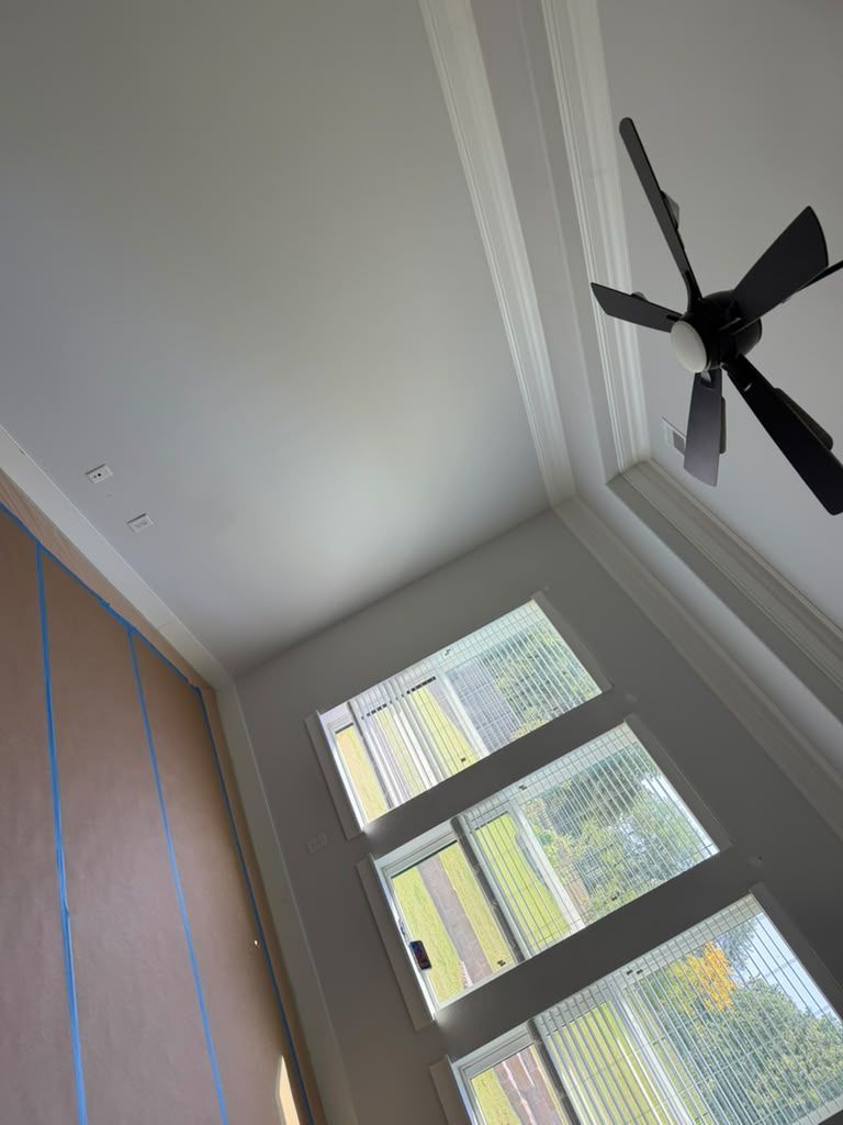 Interior room ceiling with a black ceiling fan, tall window, and a wooden cabinet edge