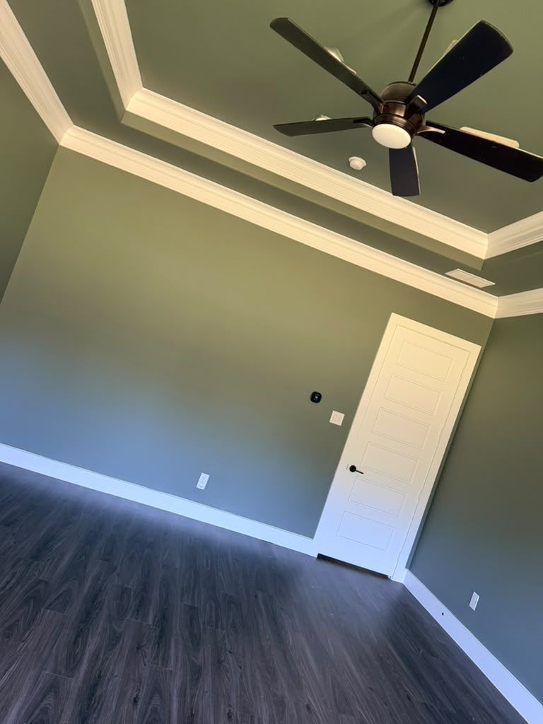 Empty gray room with tray ceiling, dark wood floor, ceiling fan, and open white door.