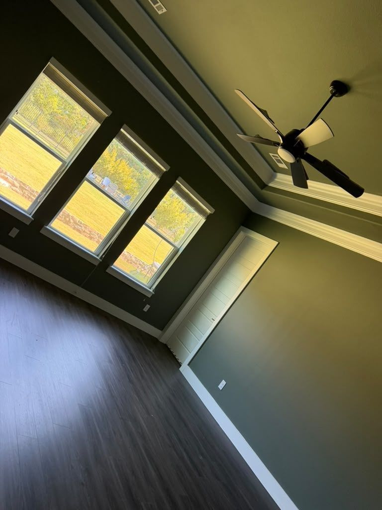 Empty room with dark wood floors, gray walls, large windows, and a ceiling fan.