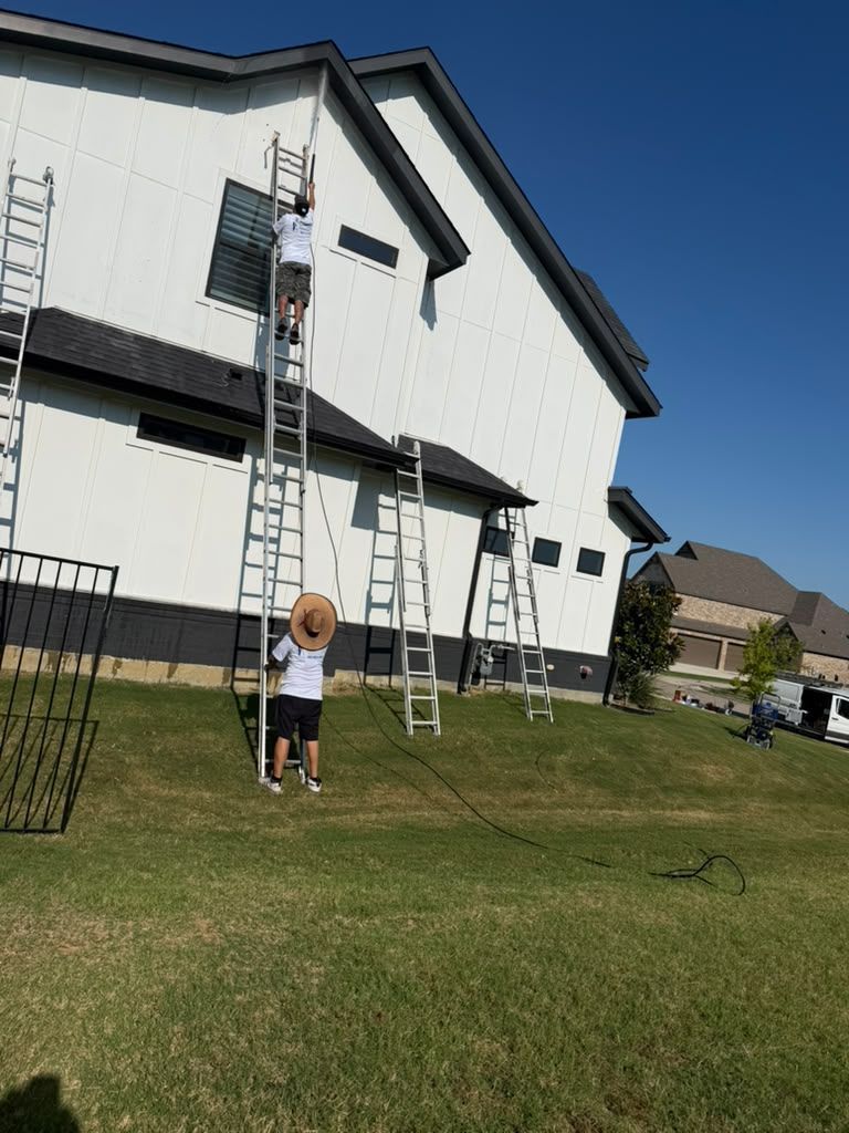 Person on a ladder painting a white house exterior on a sunny lawn.