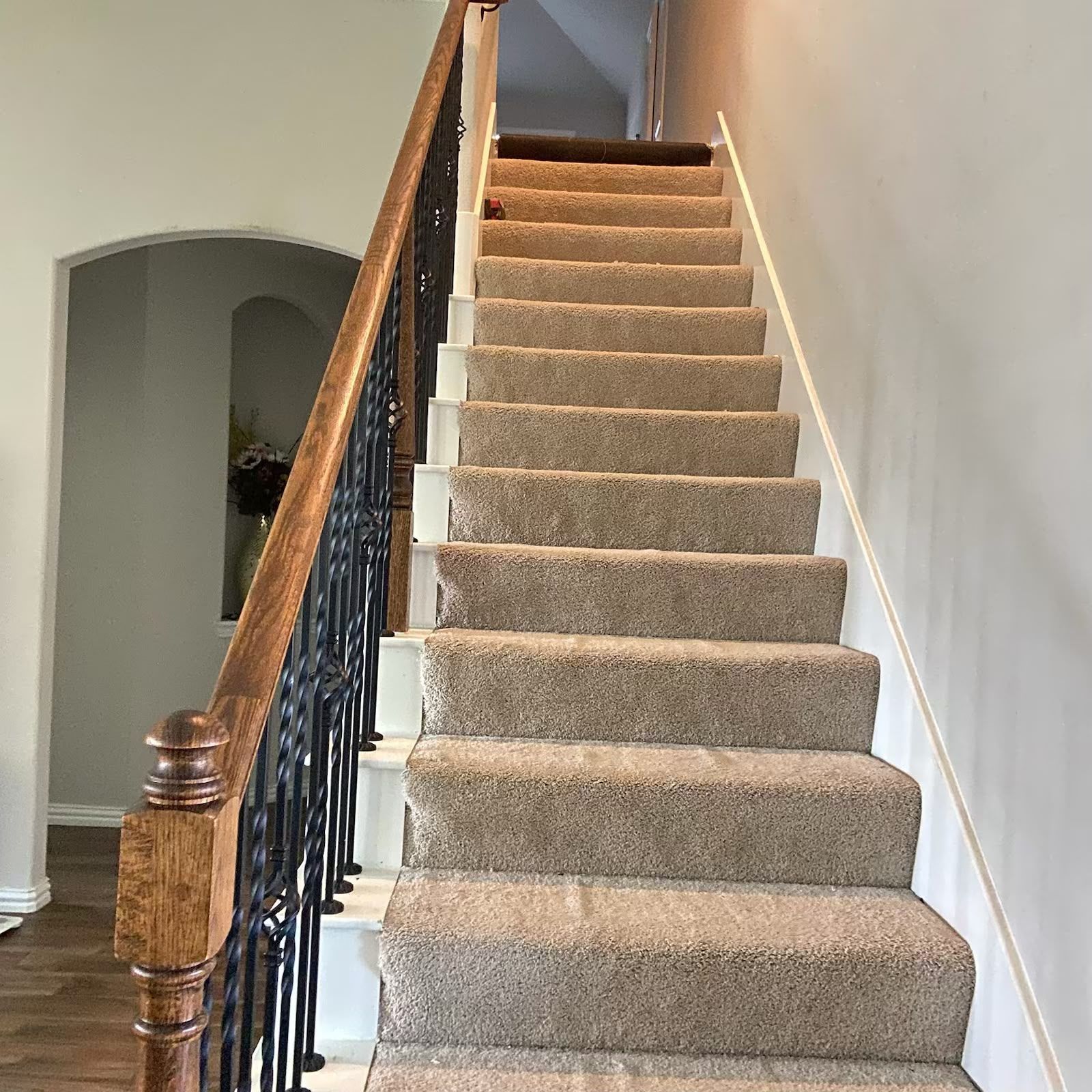 Carpeted indoor staircase with wooden banister and black wrought-iron railing in a home hallway