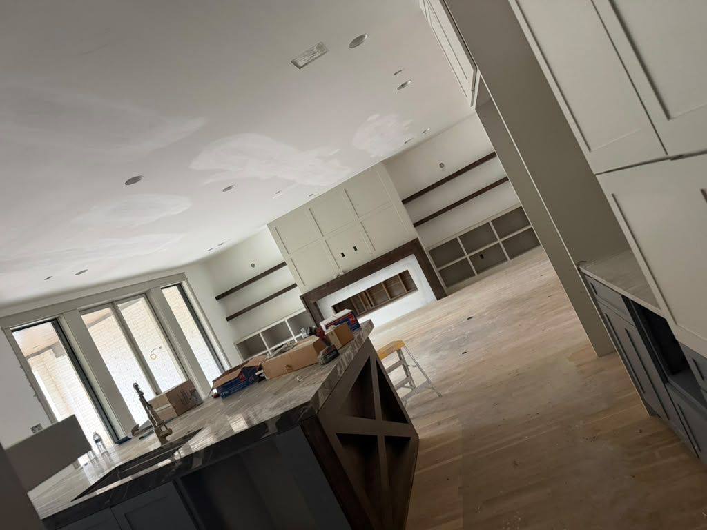 Bright, empty modern kitchen with white cabinets, large windows, and a central island under construction