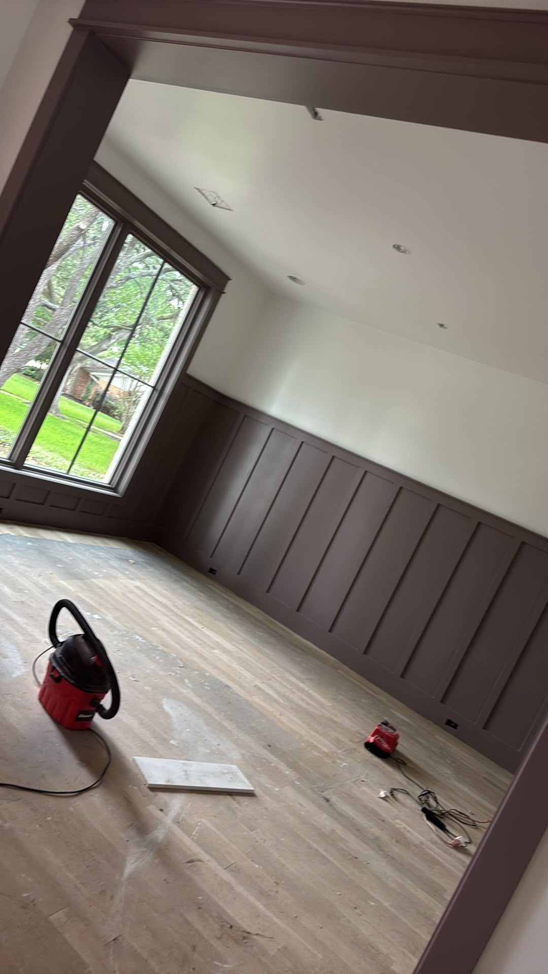 Renovated room with wood floor, gray paneling, French doors, and a vacuum on the floor