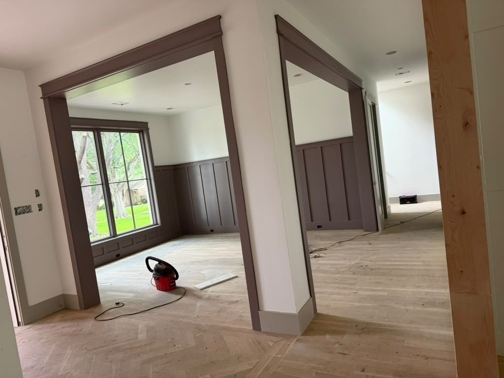 Empty room with fresh flooring, white walls, and a vacuum cleaner near glass doors.