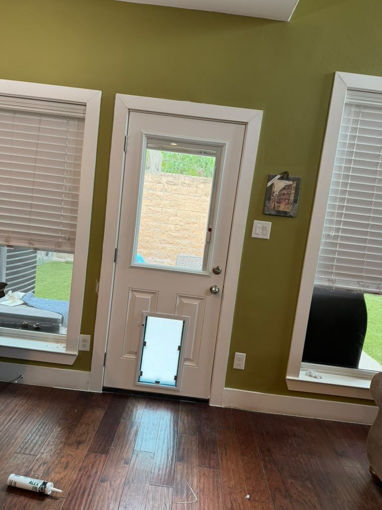 Interior view of a room with a white back door, windows with blinds, green walls, and dark hardwood floors.